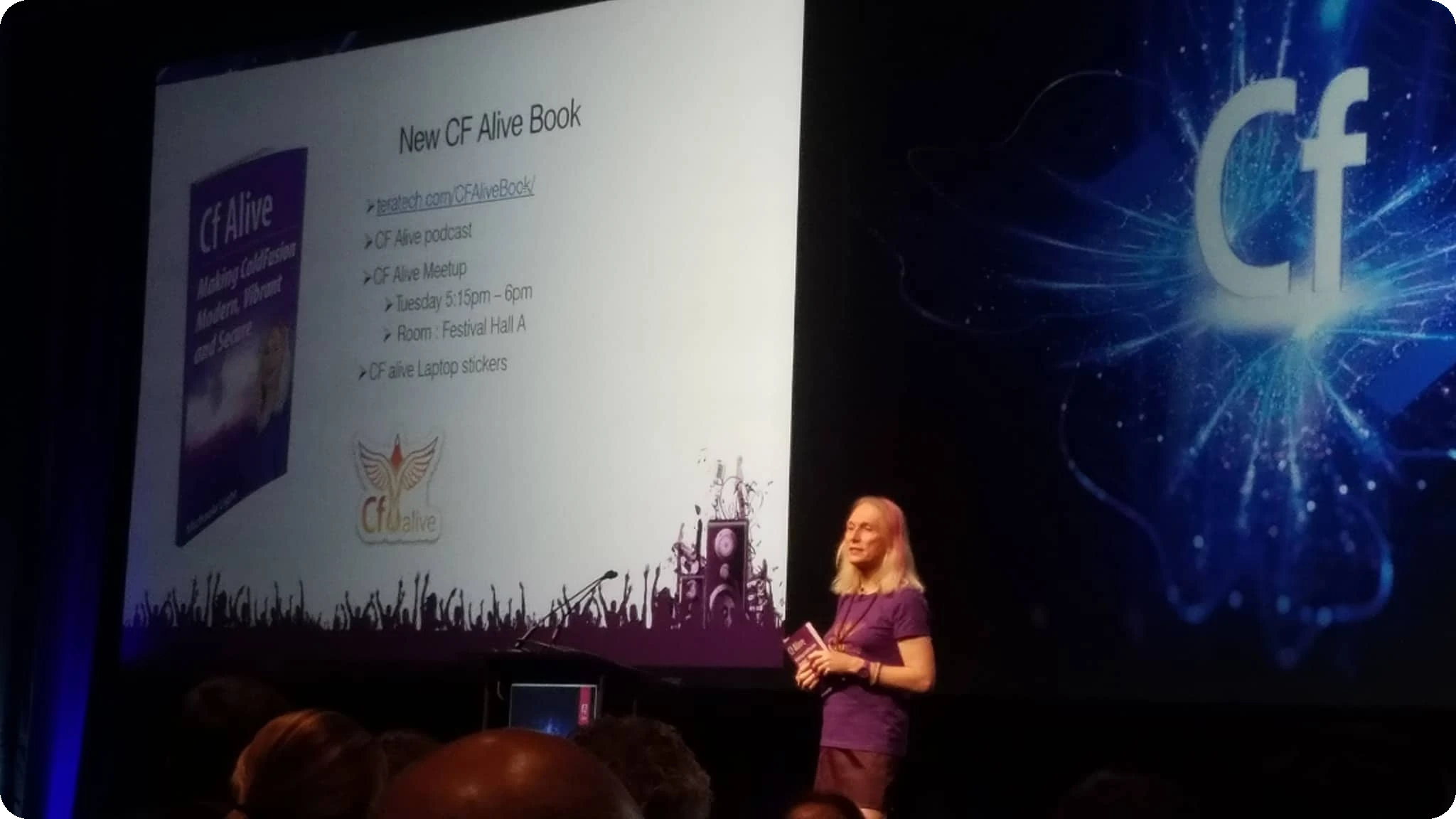 A Woman Speaker Presenting At A Conference With A Large Screen Displaying The Cf Alive Book Details.